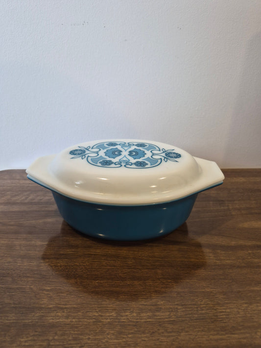 A blue and white ceramic casserole dish with a lid, featuring a blue floral pattern on the lid, resting on a dark wood surface.