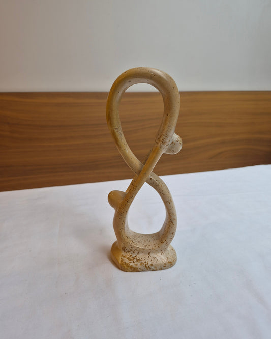 Ceramic sculpture of an infinity symbol on a white surface with a wooden base.
