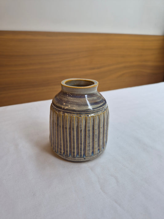 Ceramic vase with ribbed texture on a white surface with wooden background