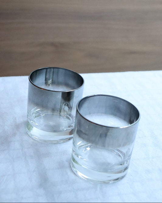 Two clear glass tumblers with silver rims on a white surface.