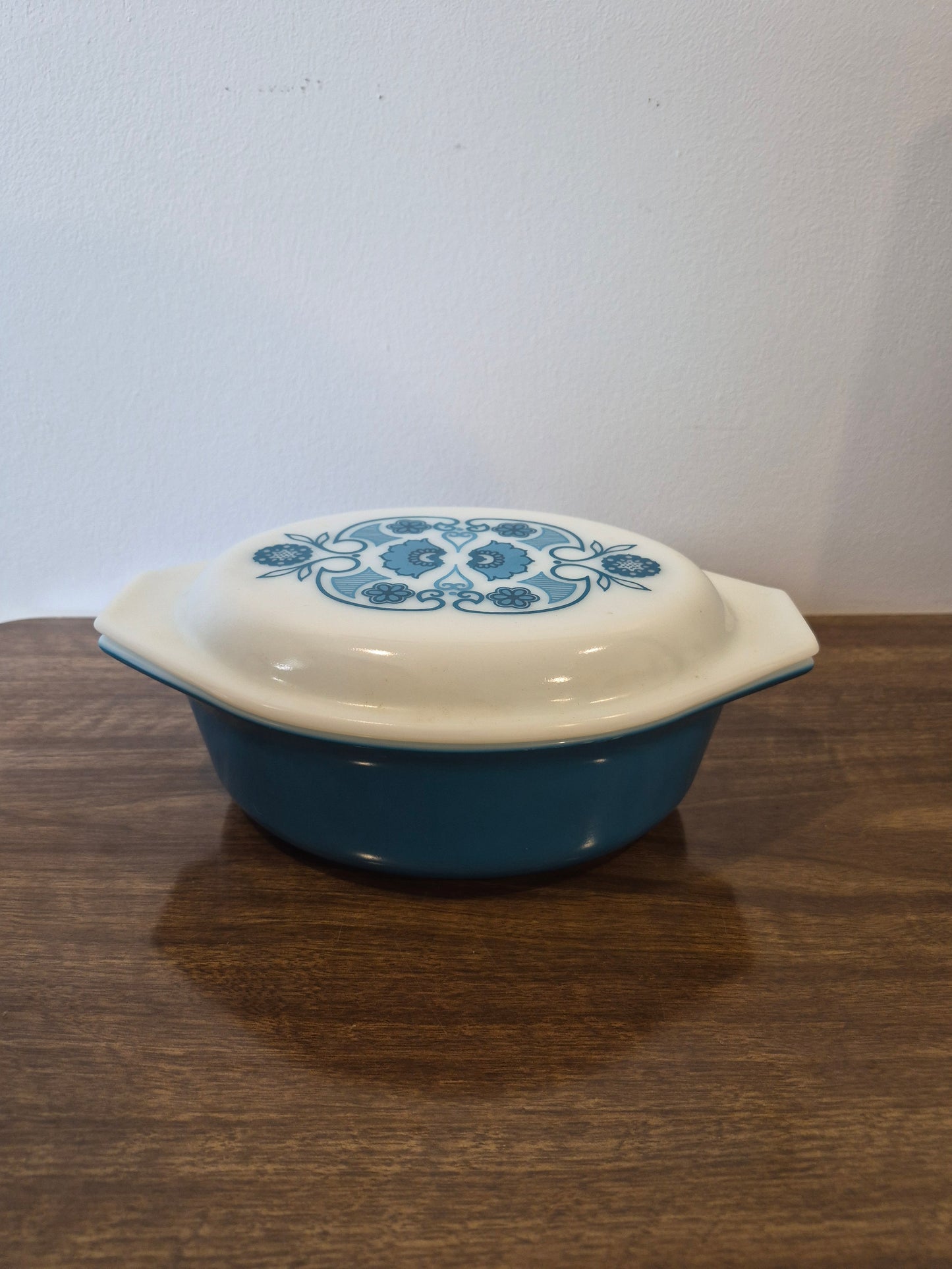 A blue and white ceramic casserole dish with a lid, featuring a blue floral pattern on the lid, resting on a dark wood surface.