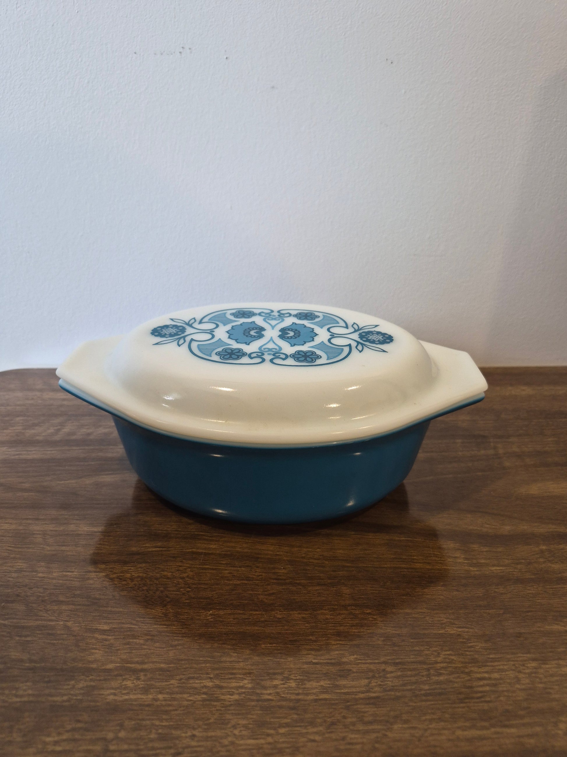A blue and white ceramic casserole dish with a lid, featuring a blue floral pattern on the lid, resting on a dark wood surface.