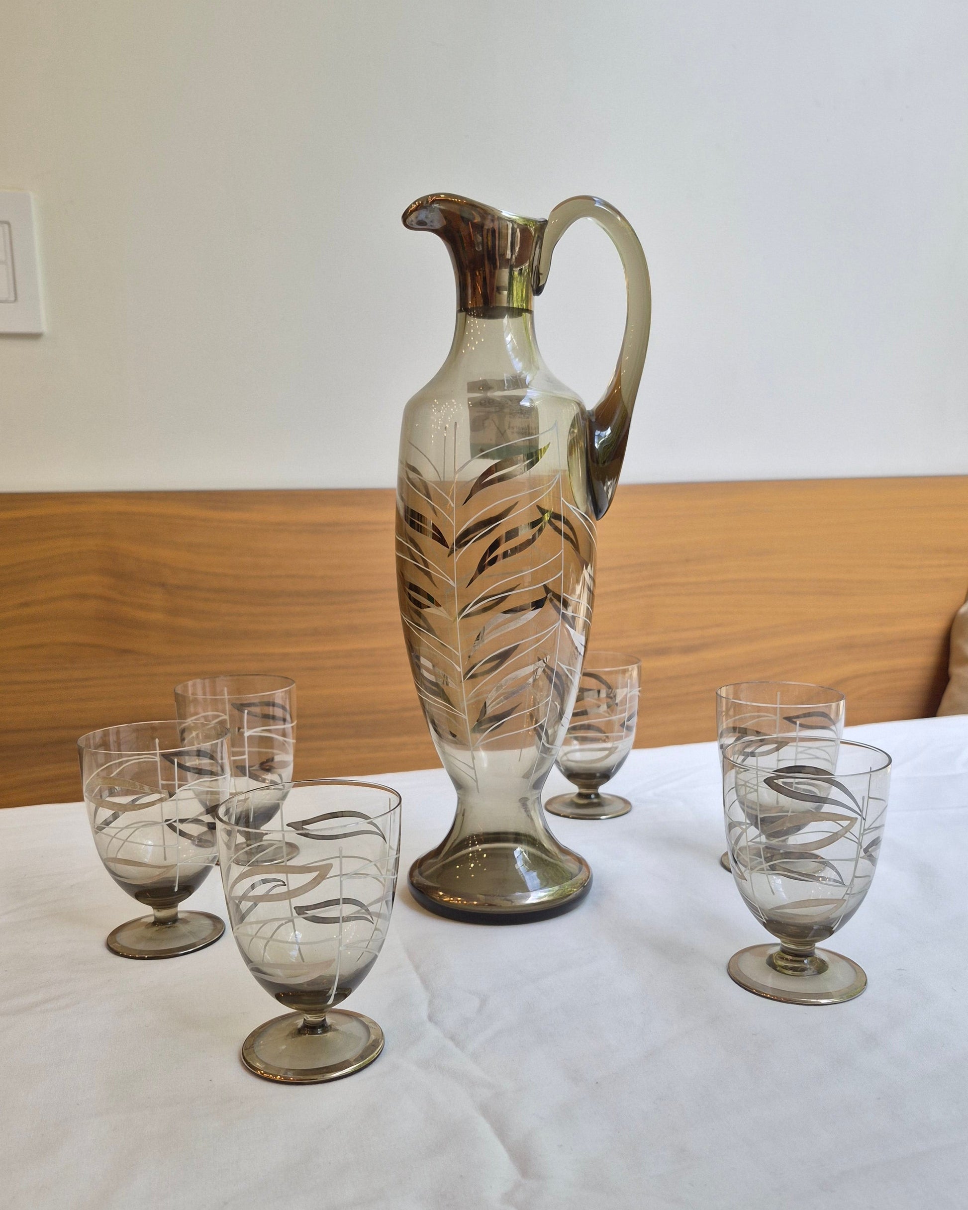 Set of glass decanters and glasses on a wooden surface with a white wall background.