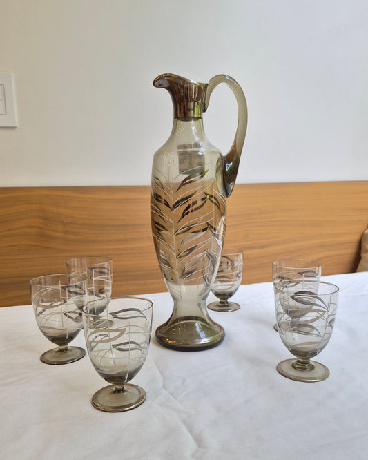 Set of glass decanters and glasses on a wooden surface with a white wall background.