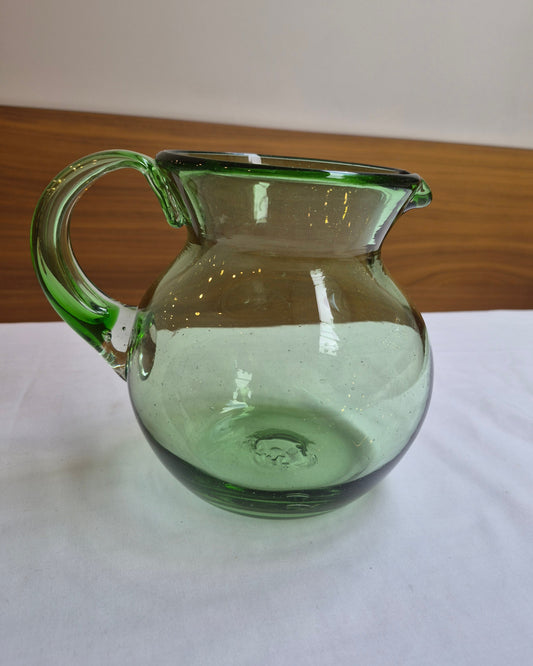 Green glass pitcher on a white surface with a wooden background