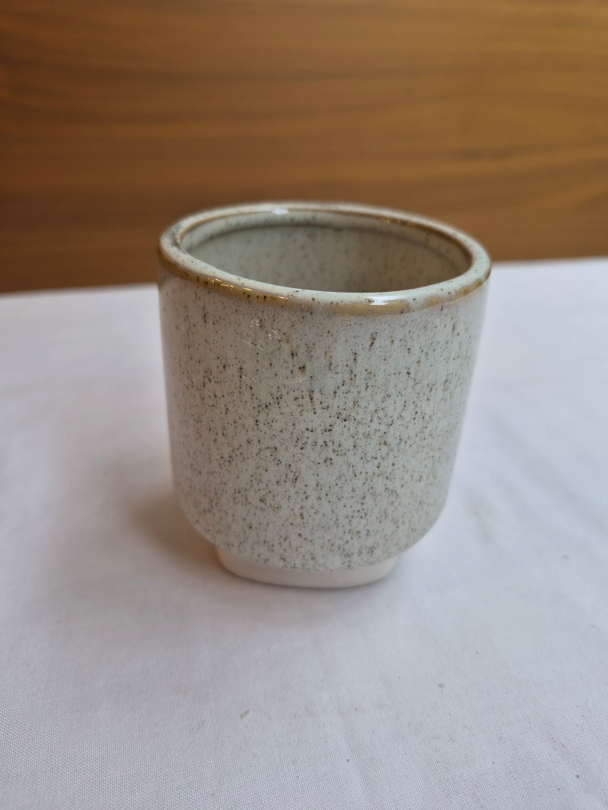 Speckled ceramic cup on a white surface with a wooden background