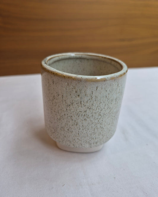 Speckled ceramic cup on a white surface with a wooden background