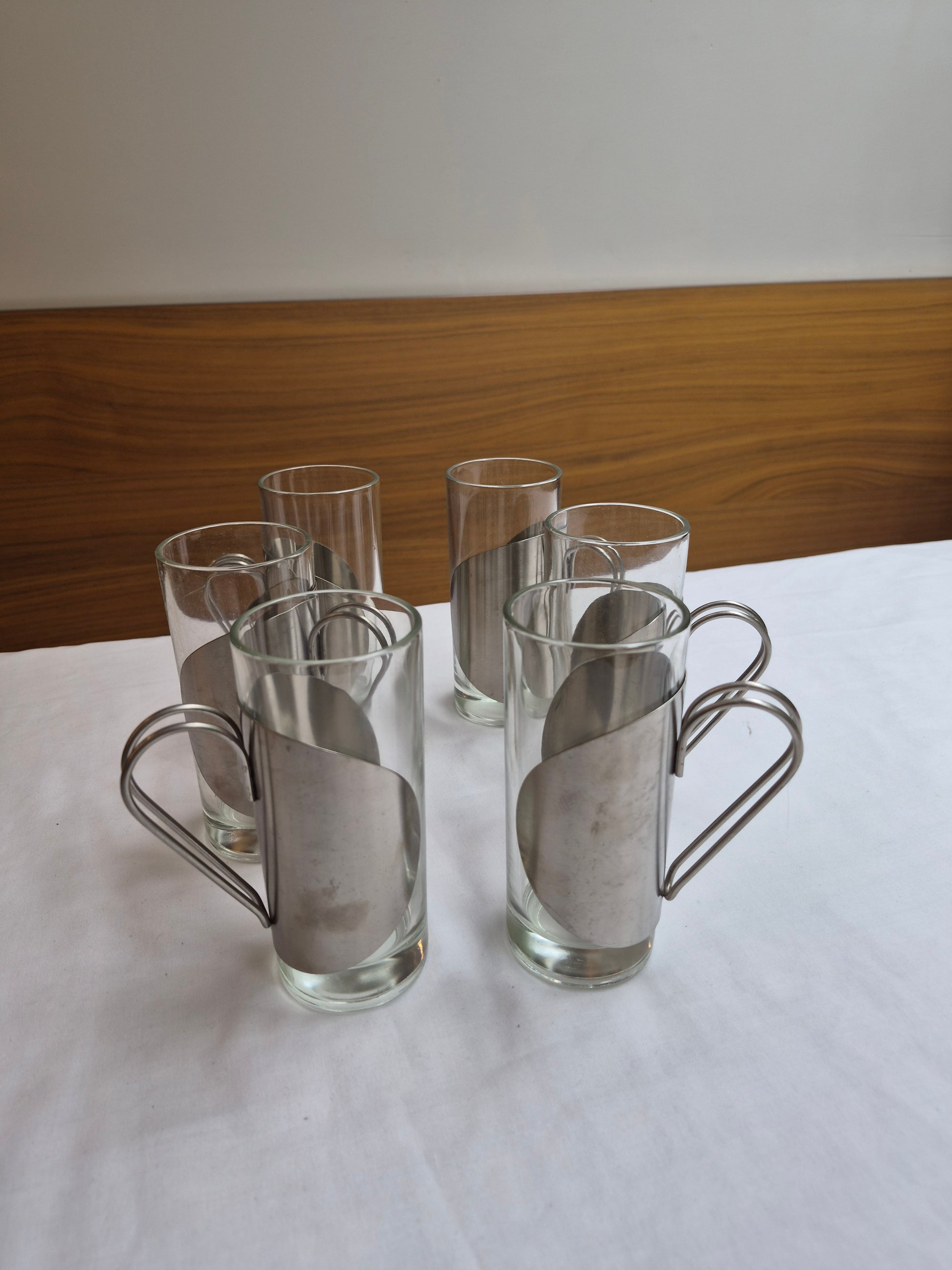 Clear glass tumblers with metal holders on a white surface.