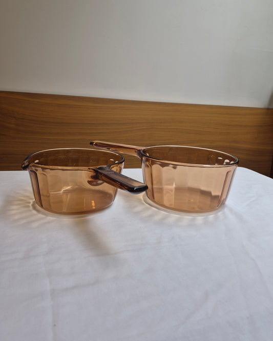 Two transparent glass bowls with wooden handles on a white surface.