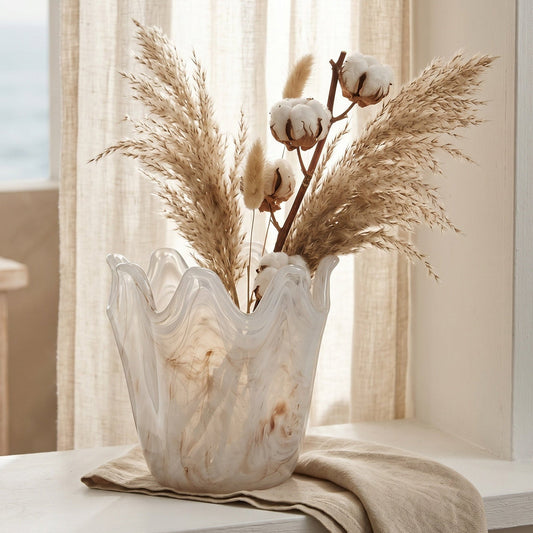 Decorative vase with cotton and pampas grass on a windowsill with a view of the ocean.
