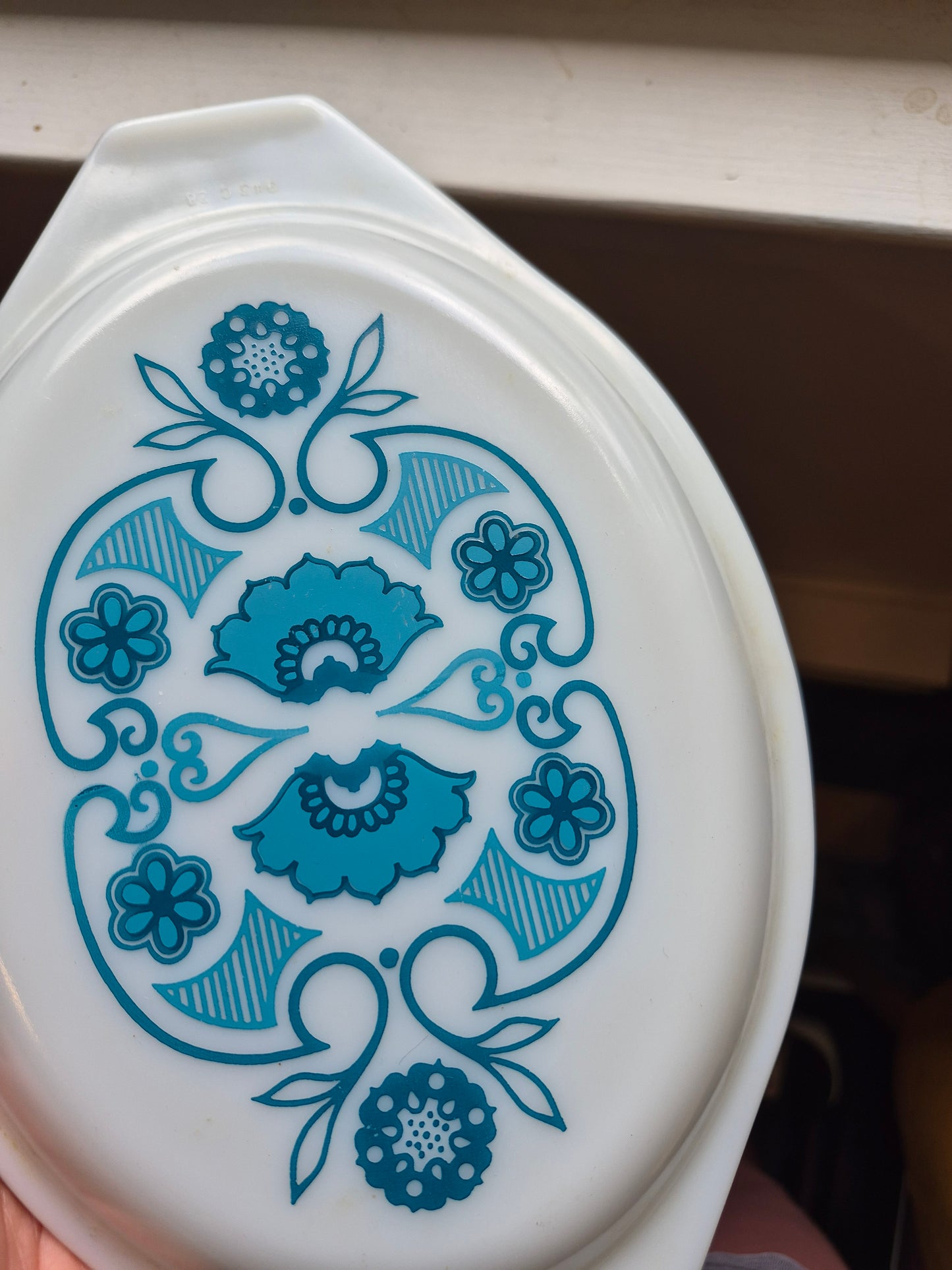A vintage white oval glass dish with a blue floral pattern, held by a hand in front of a light-colored surface.